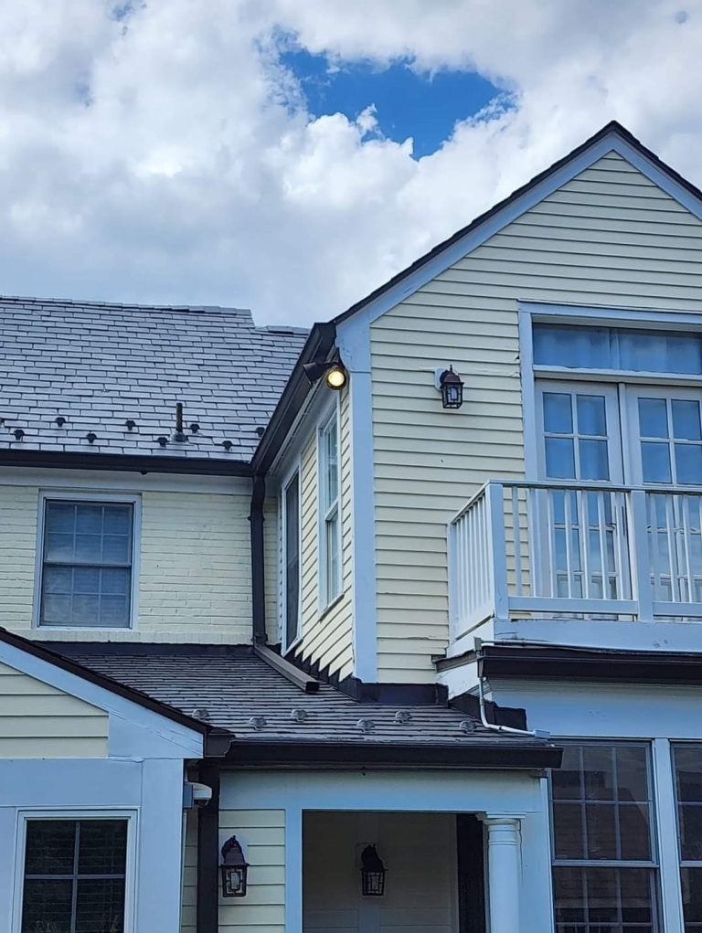 Two-story house with light siding and white trim under a blue sky with clouds.