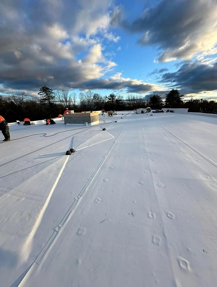 Workers installing a white membrane roofing system under a blue sky.