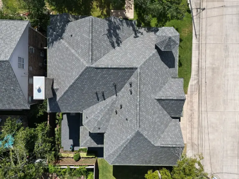 Aerial view of a large shingle roof on a suburban home in a green neighborhood.