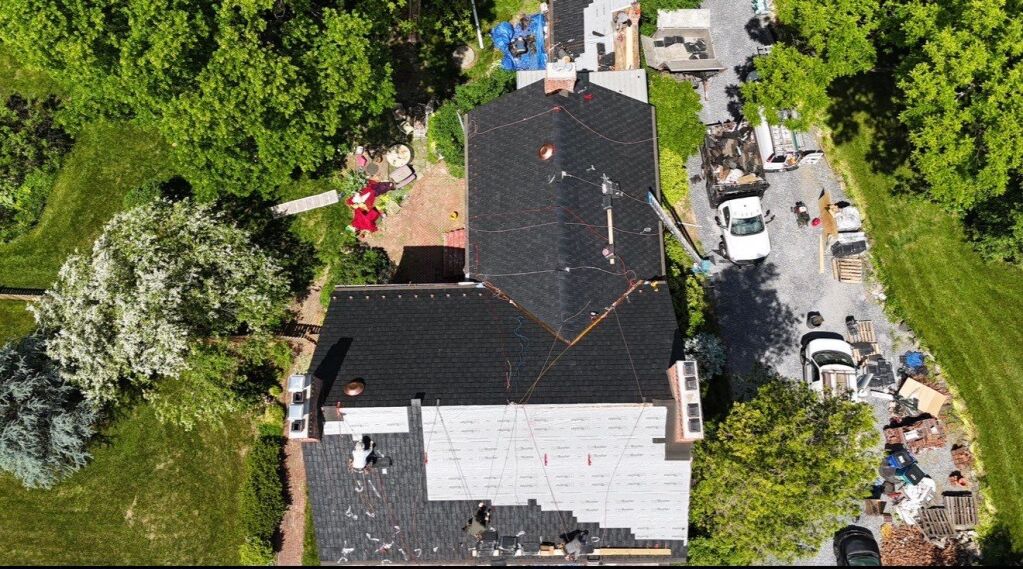 Aerial view of a house with ongoing roof renovation, surrounded by greenery.