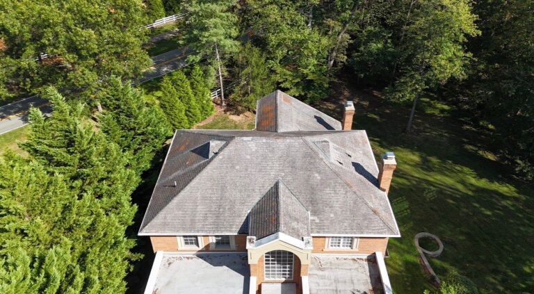 Aerial view of a large suburban house with a gray roof surrounded by trees.