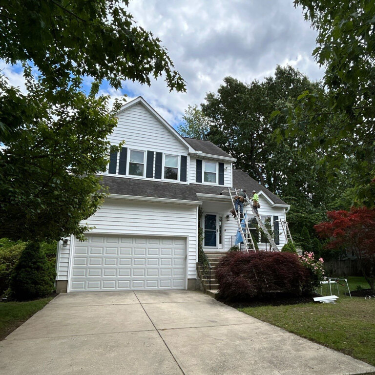 Suburban house with workers on ladders doing exterior work on a cloudy day.
