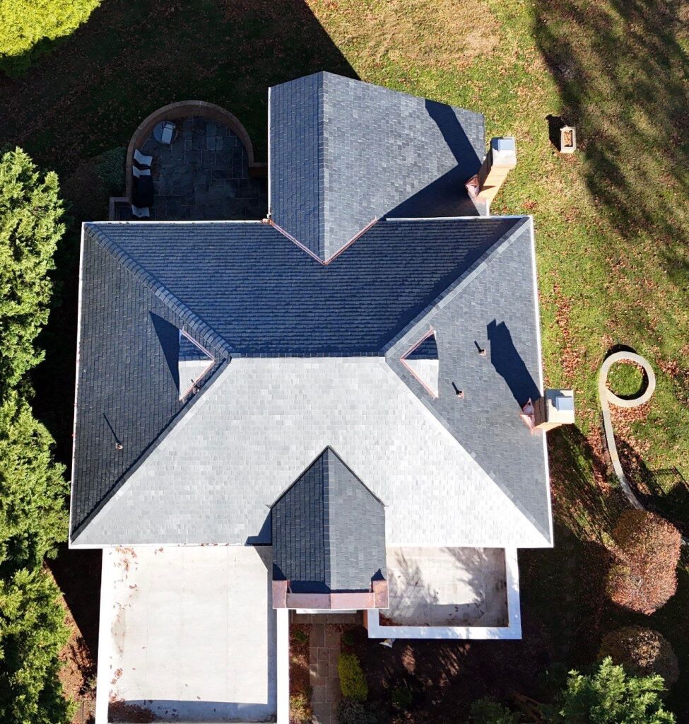 Aerial view of a house with a new dark shingle roof and surrounding garden.