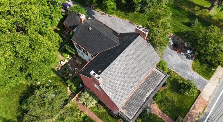 Aerial view of a brick house with a black roof surrounded by green trees.