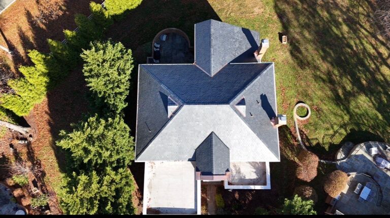 Aerial view of a modern house with a complex roof and surrounding greenery.