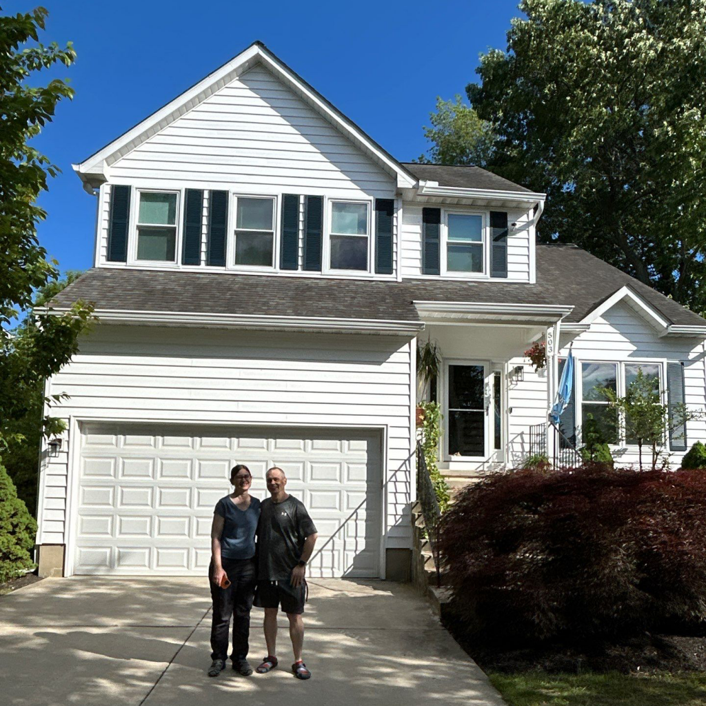 Couple standing outside a two-story white house under a clear blue sky