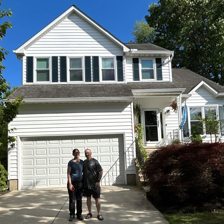 Two people standing in front of a white suburban house with a garage
