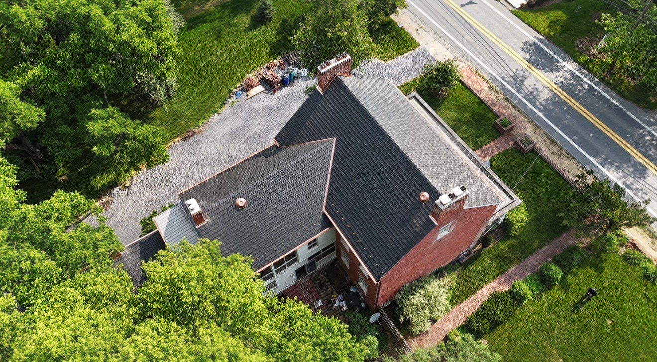 Aerial view of a large brick house surrounded by greenery and a road.