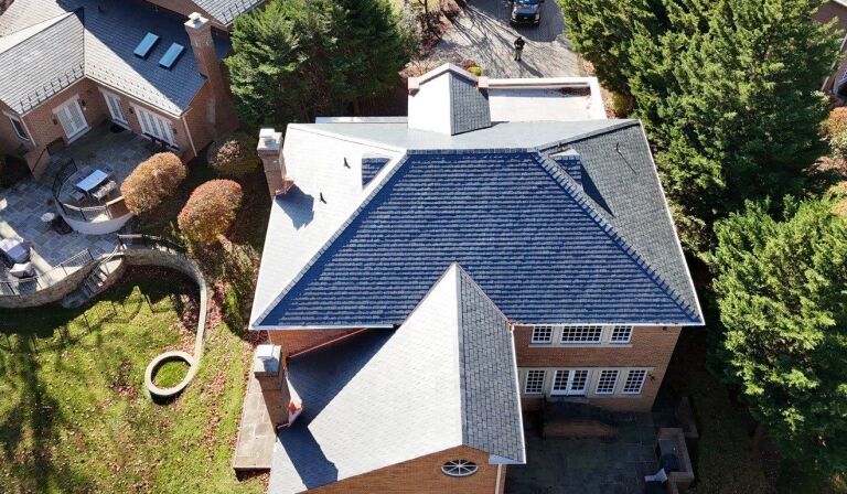 Aerial view of a house with a dark shingle roof surrounded by a garden