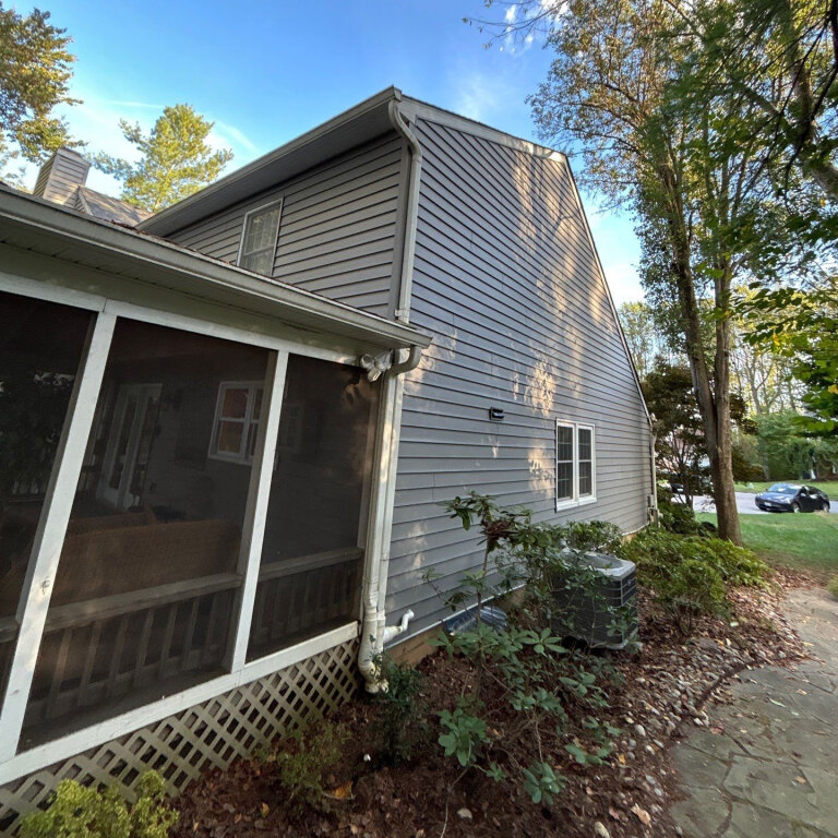 Side view of house with gray siding and trees in the background