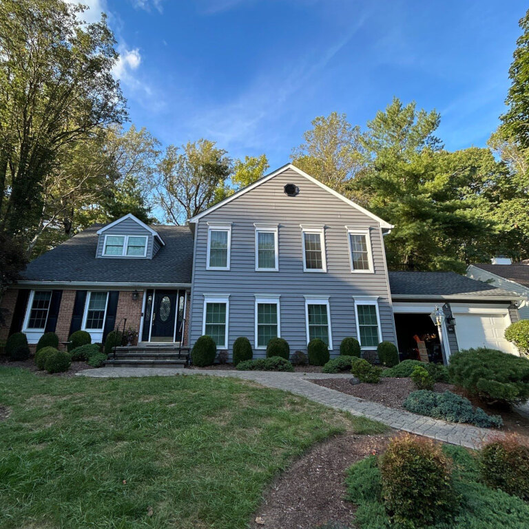 Charming two-story suburban house with gray siding and lush landscaping