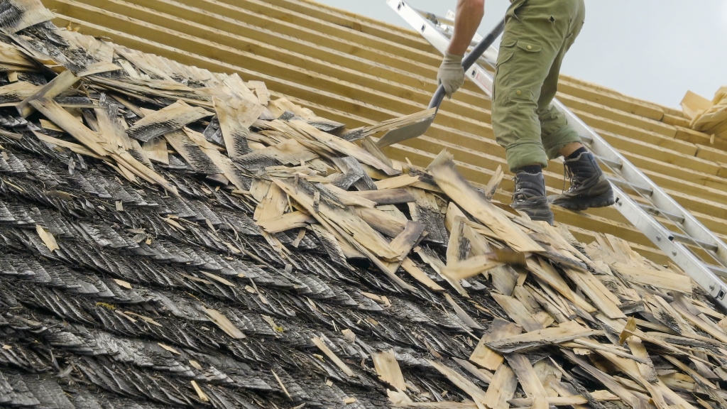 Worker renovating a wooden shingle roof with a ladder and tools