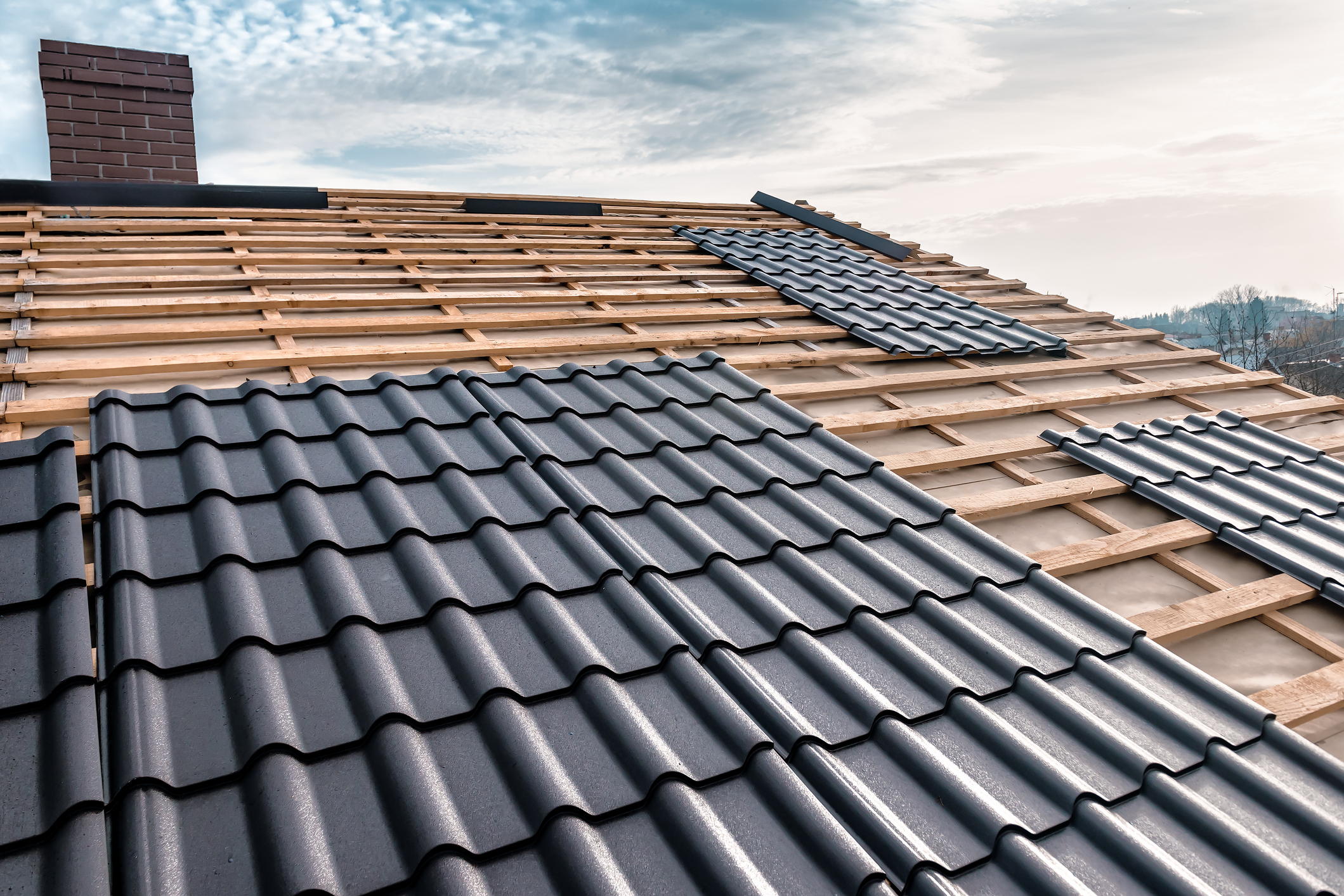Roof installation with black metal tiles in progress under a cloudy sky.