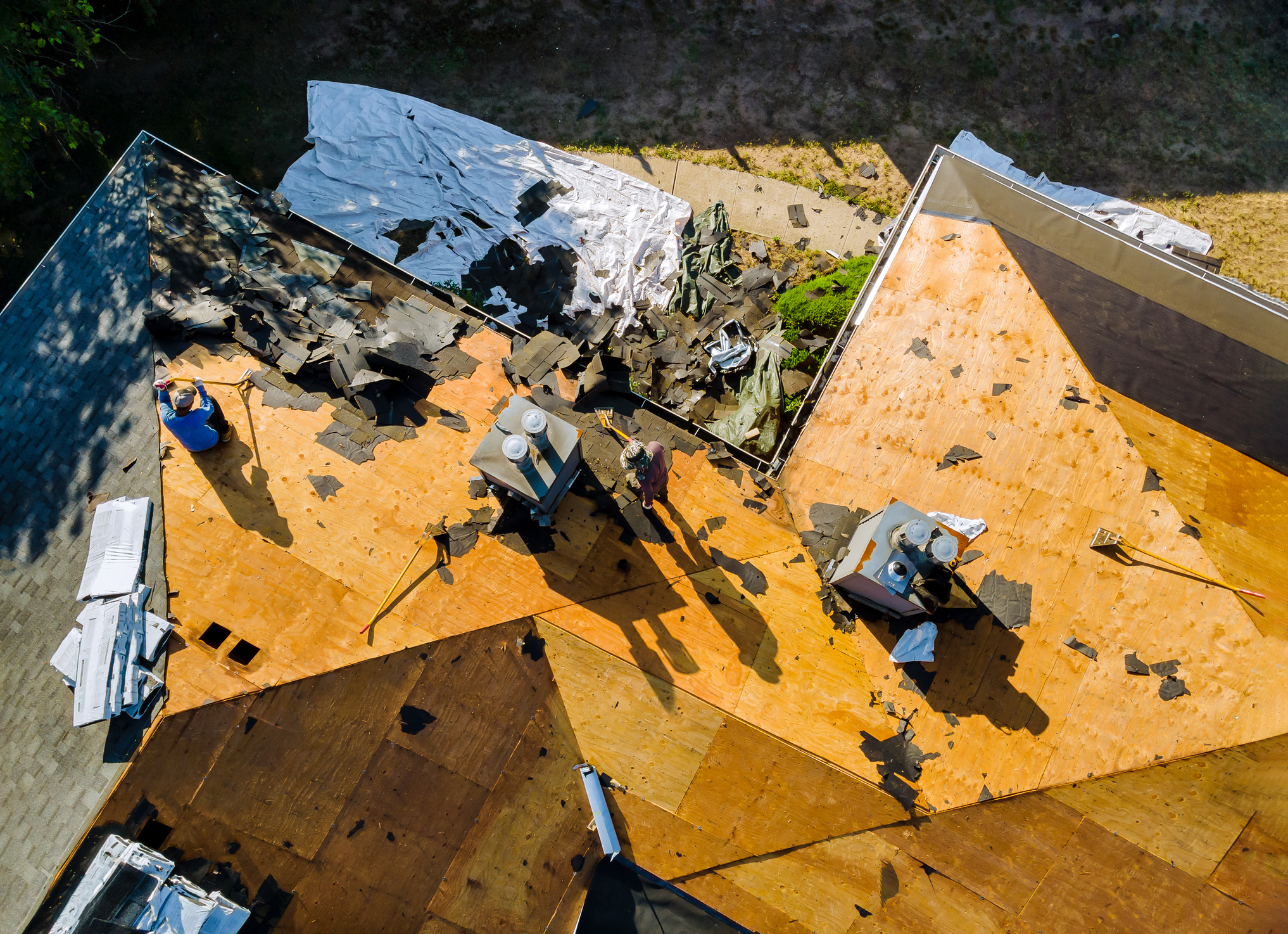 Aerial view of roof renovation with workers removing old shingles.