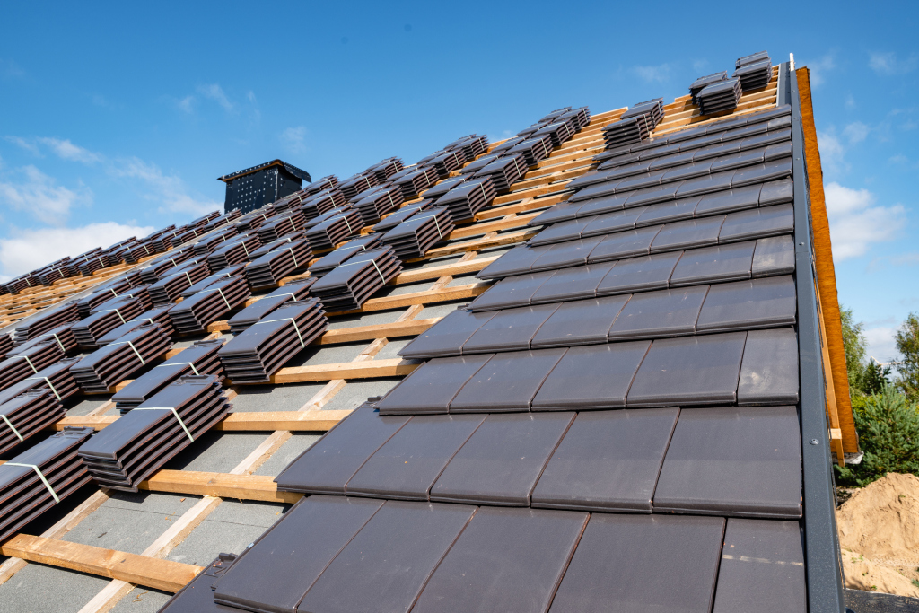 New roof construction with stacked black tiles against blue sky