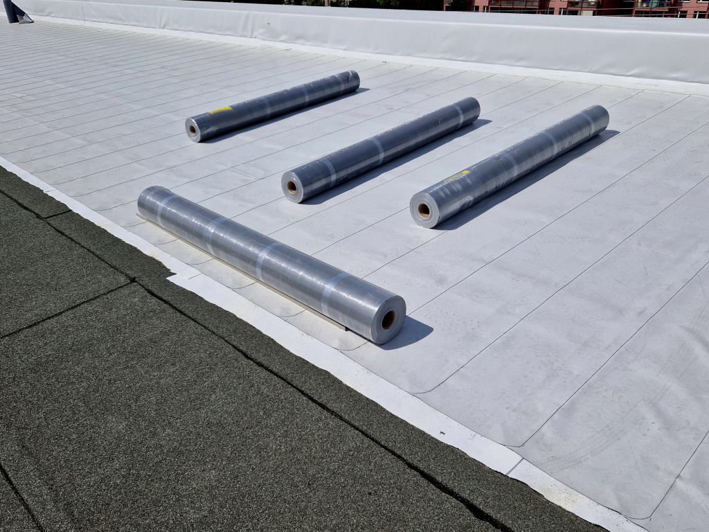 Four rolls of roofing membrane on a flat roof surface.