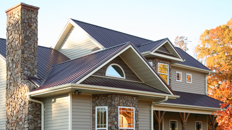 Modern house with stone chimney and metal roof in autumn setting.