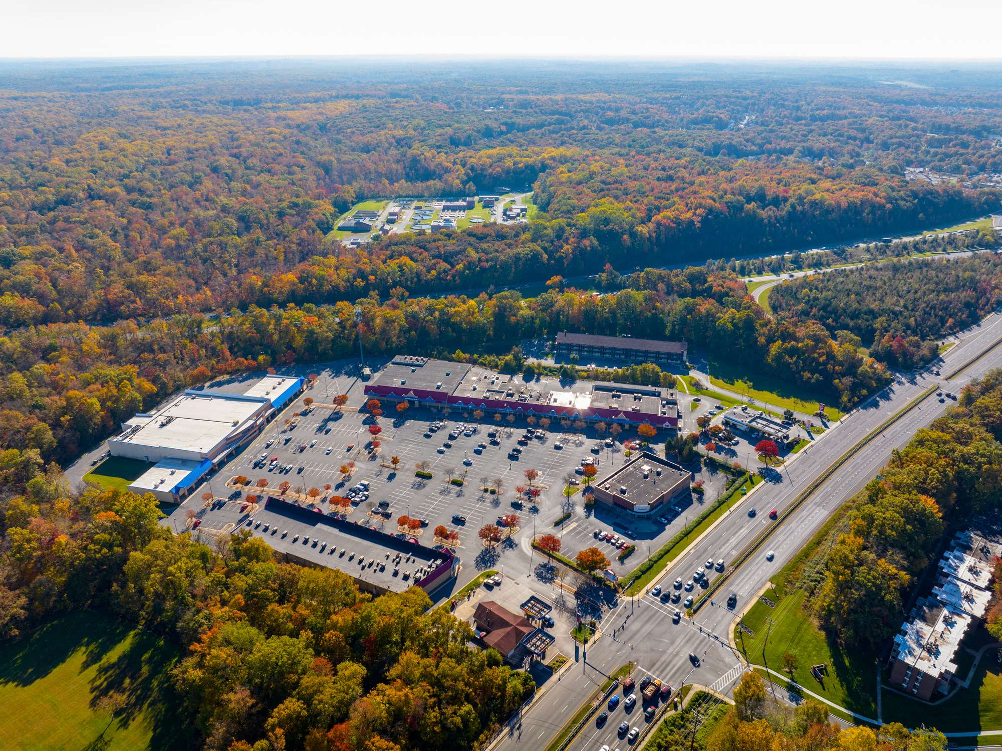 Aerial view of a shopping center surrounded by autumn foliage and parking lot
