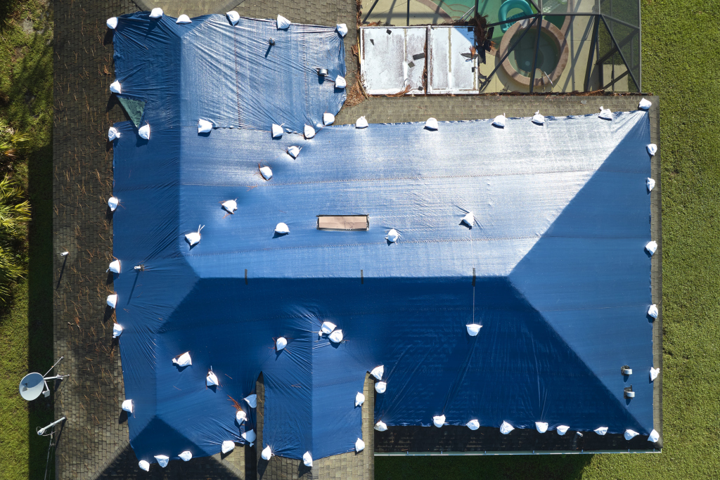 Aerial view of a roof covered with a blue tarp after storm damage.