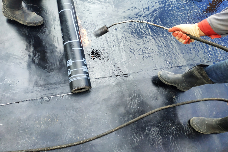 Worker applying torch-down roofing membrane with flame
