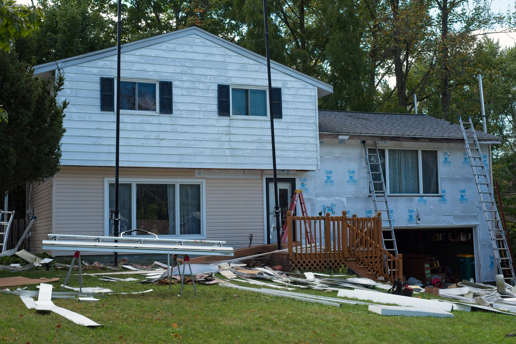 Residential house undergoing siding renovation with scattered materials.