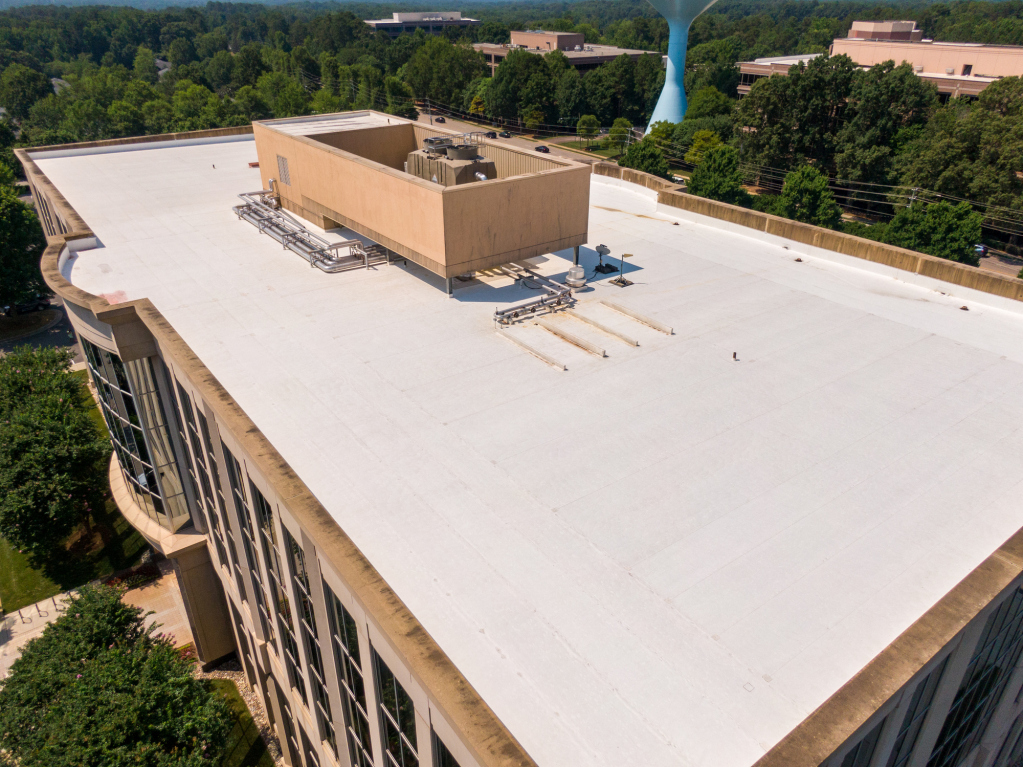 Aerial view of a large white building roof with surrounding greenery.