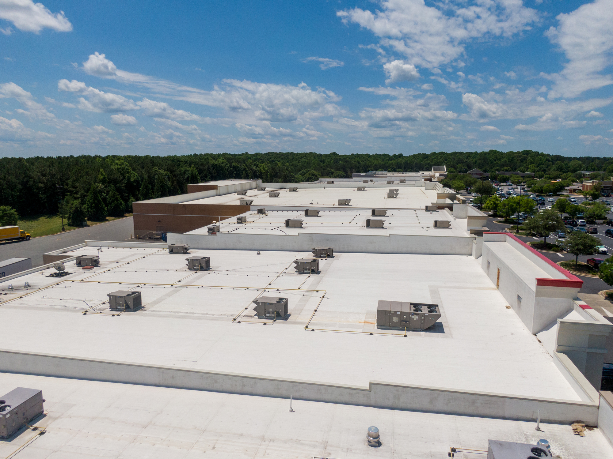 Aerial view of a large white flat rooftop with HVAC units under a blue sky.