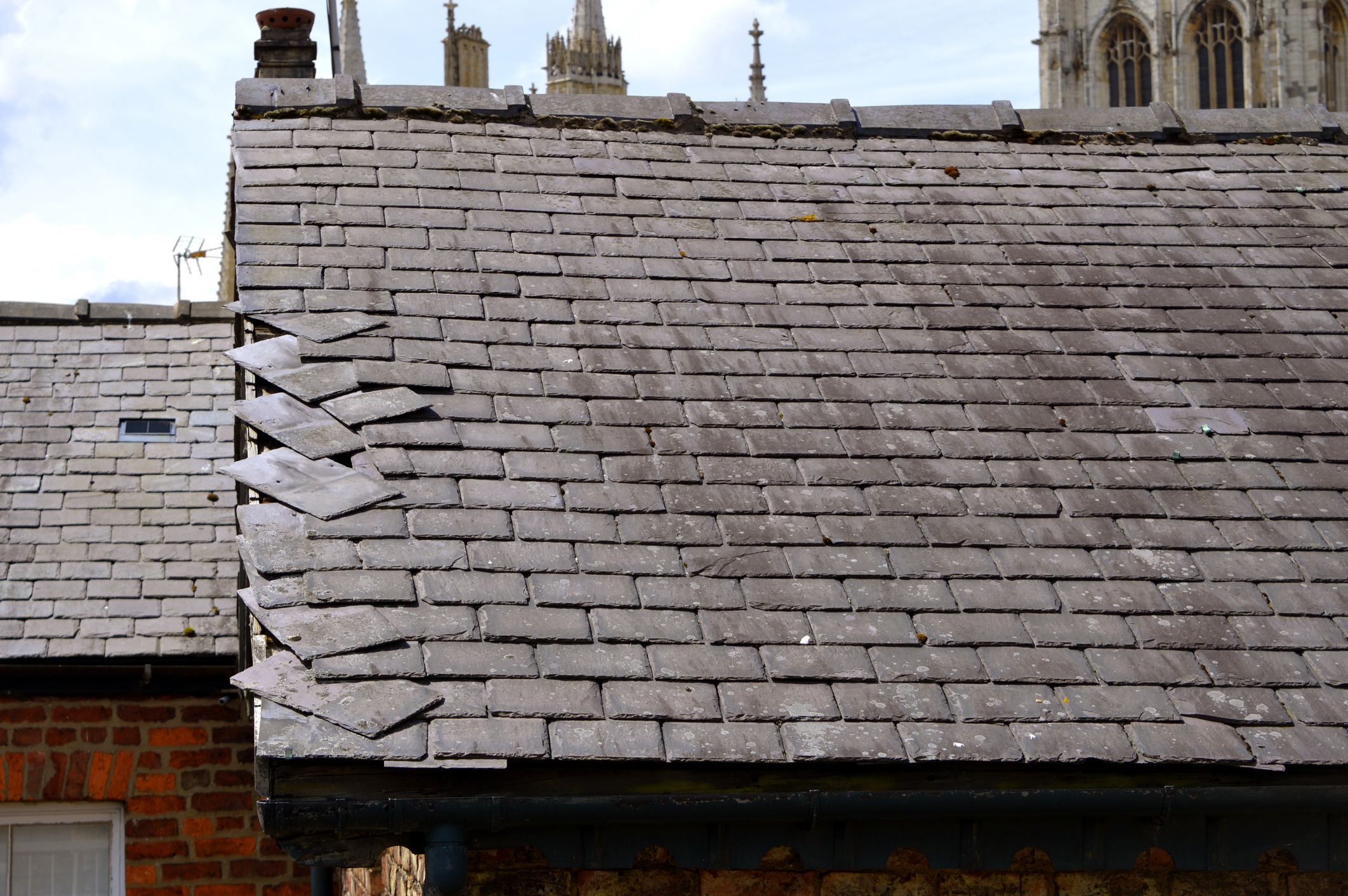 Close-up of a weathered roof with loose slate tiles.